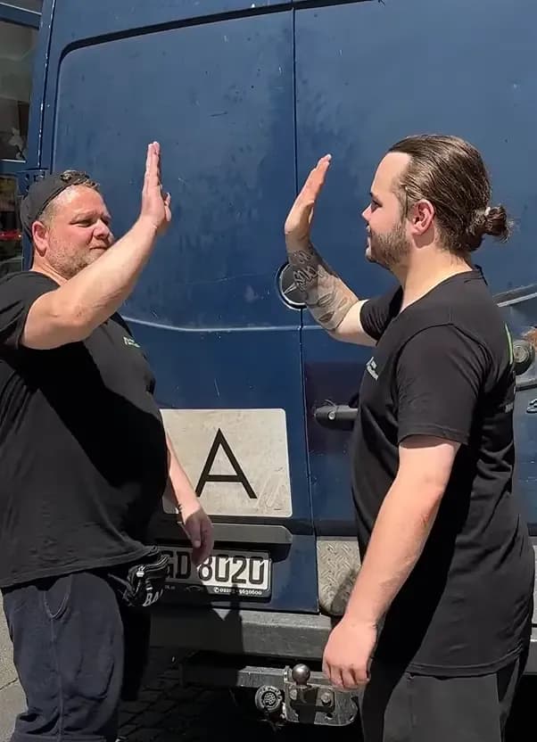 Zwei Mitarbeiter von NRW Haushaltsauflösung beim High-Five vor dem Transporter