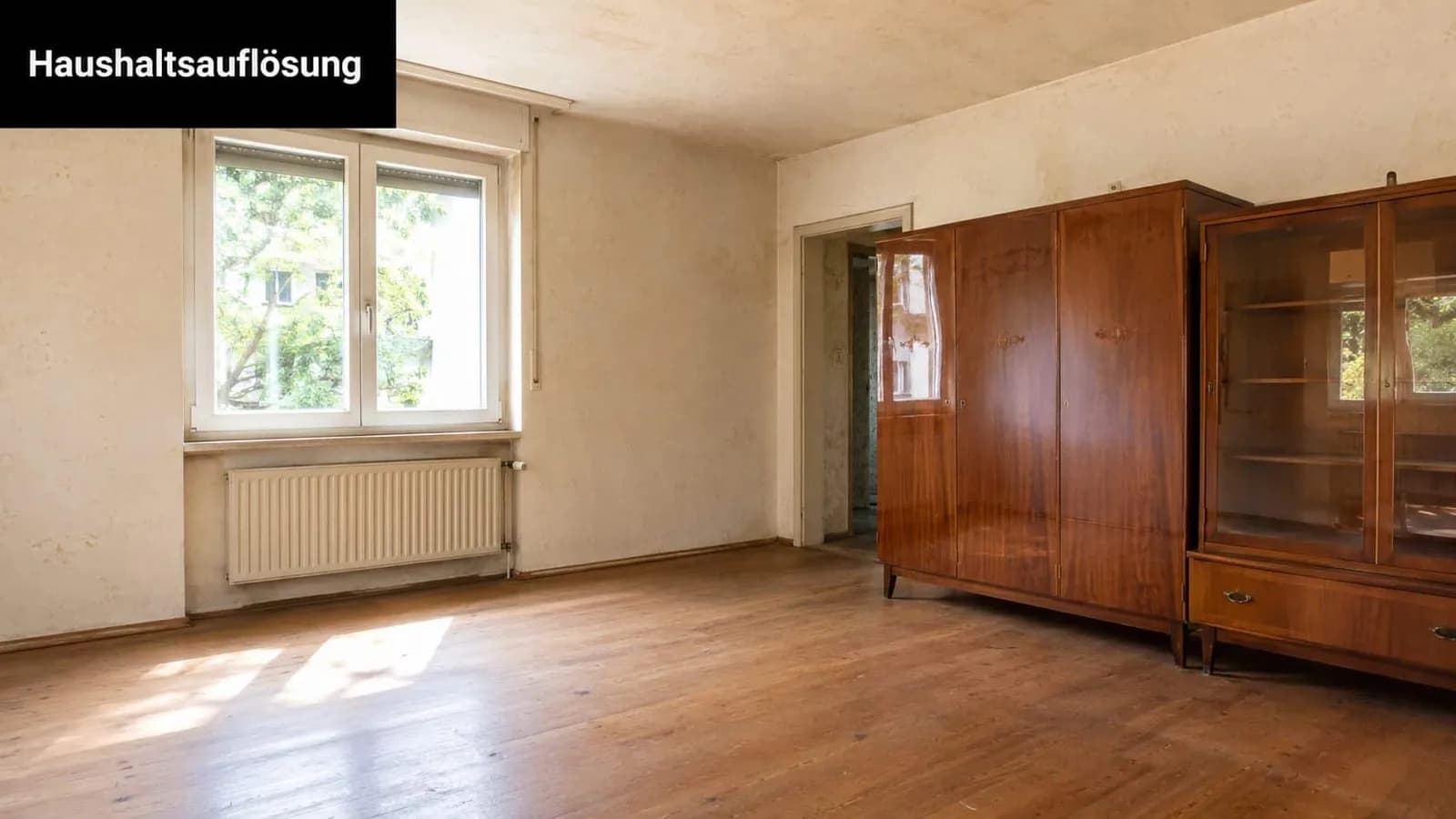Ein helles Zimmer mit einem großen Holzschrank vor einer leeren Wand in einer Wohnung zur Haushaltsauflösung.