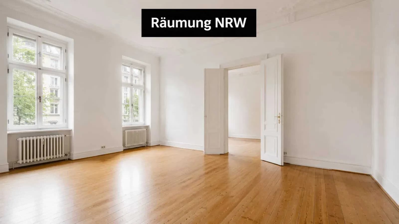 Ein heller, leerer Raum mit Holzboden, hohen Fenstern und einer offenen Doppeltür in einer Altbauwohnung.